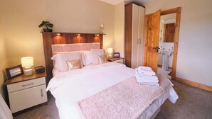 A bedroom with a bed, nightstands, a wooden wardrobe, a bedside table with a lamp, and a bathroom visible through an open door.