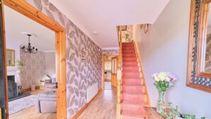 A wooden staircase leading to a second floor, a living room with a sofa and a fireplace, and a hallway with patterned wallpaper.
