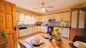 A kitchen with wooden cabinets, a dining table set with plates, glasses, and a bottle of wine, and a ceiling fan.
