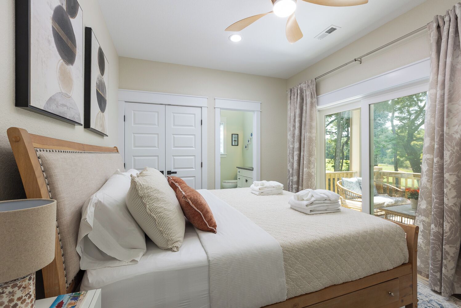 Une chambre à coucher avec un lit, un ventilateur de plafond, une grande fenêtre avec des rideaux et une porte.