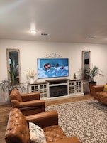 Una sala de estar con chimenea, sofás de cuero, televisor y espejos decorativos.