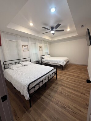 A bedroom with two beds, a ceiling fan, and a large window with blinds.
