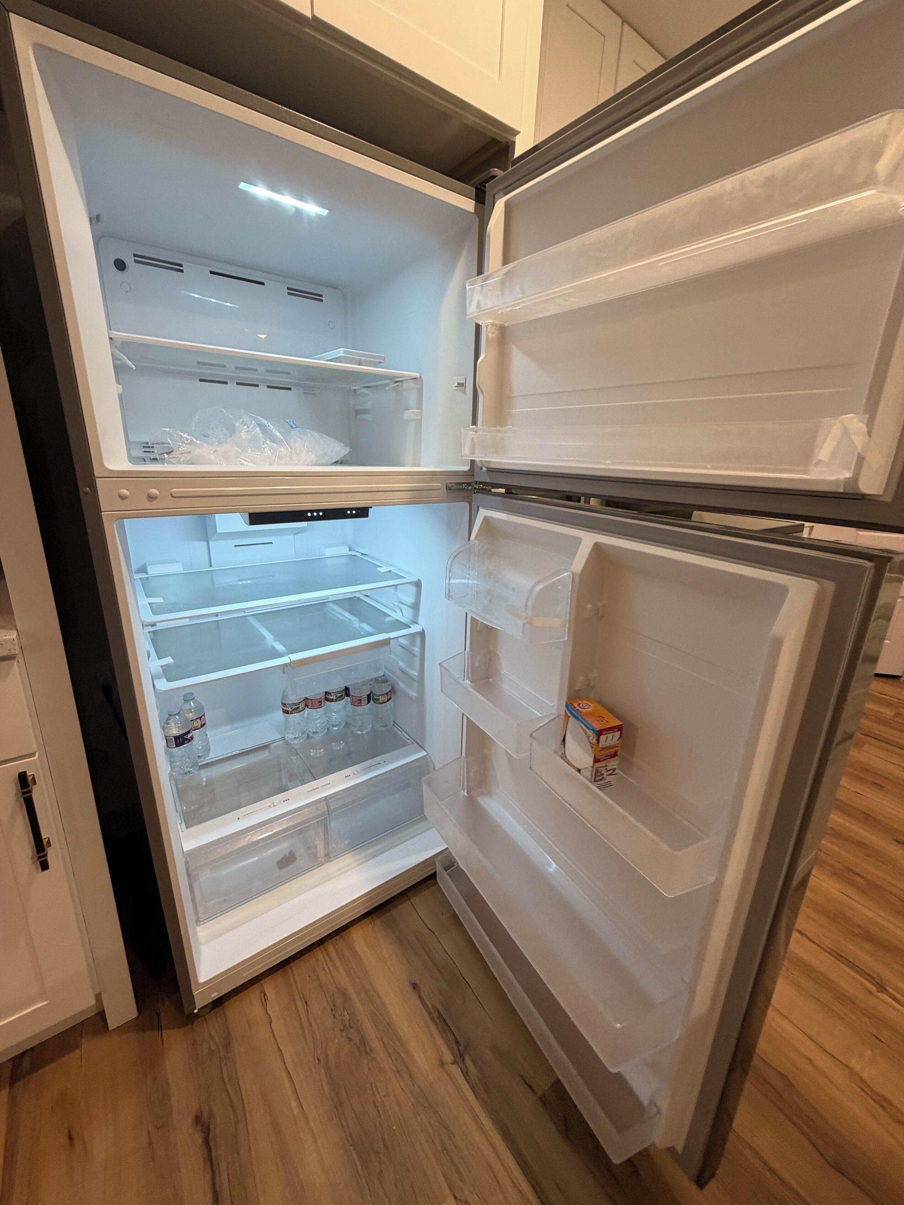 Un refrigerador abierto con varios estantes y compartimentos, algunos conteniendo recipientes de plástico y botellas.