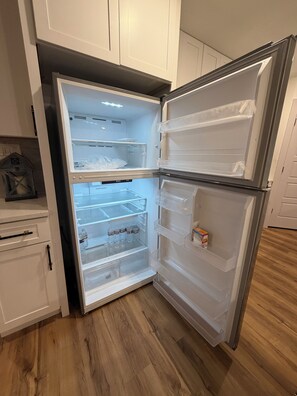 A kitchen with a double-door refrigerator, wooden flooring, and white cabinets.