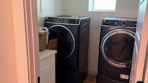 A laundry room with two stacked front-loading washers and dryers, a small window, and a white cabinet. - The Rustic Charm (Midlothian)