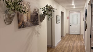 A hallway with wooden flooring, a white door, and wall-mounted decorations including a plant and a picture. - The Rustic Charm (Midlothian)
