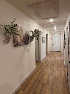 A hallway with wooden flooring, a white door, and wall-mounted decorations including a plant and a picture.