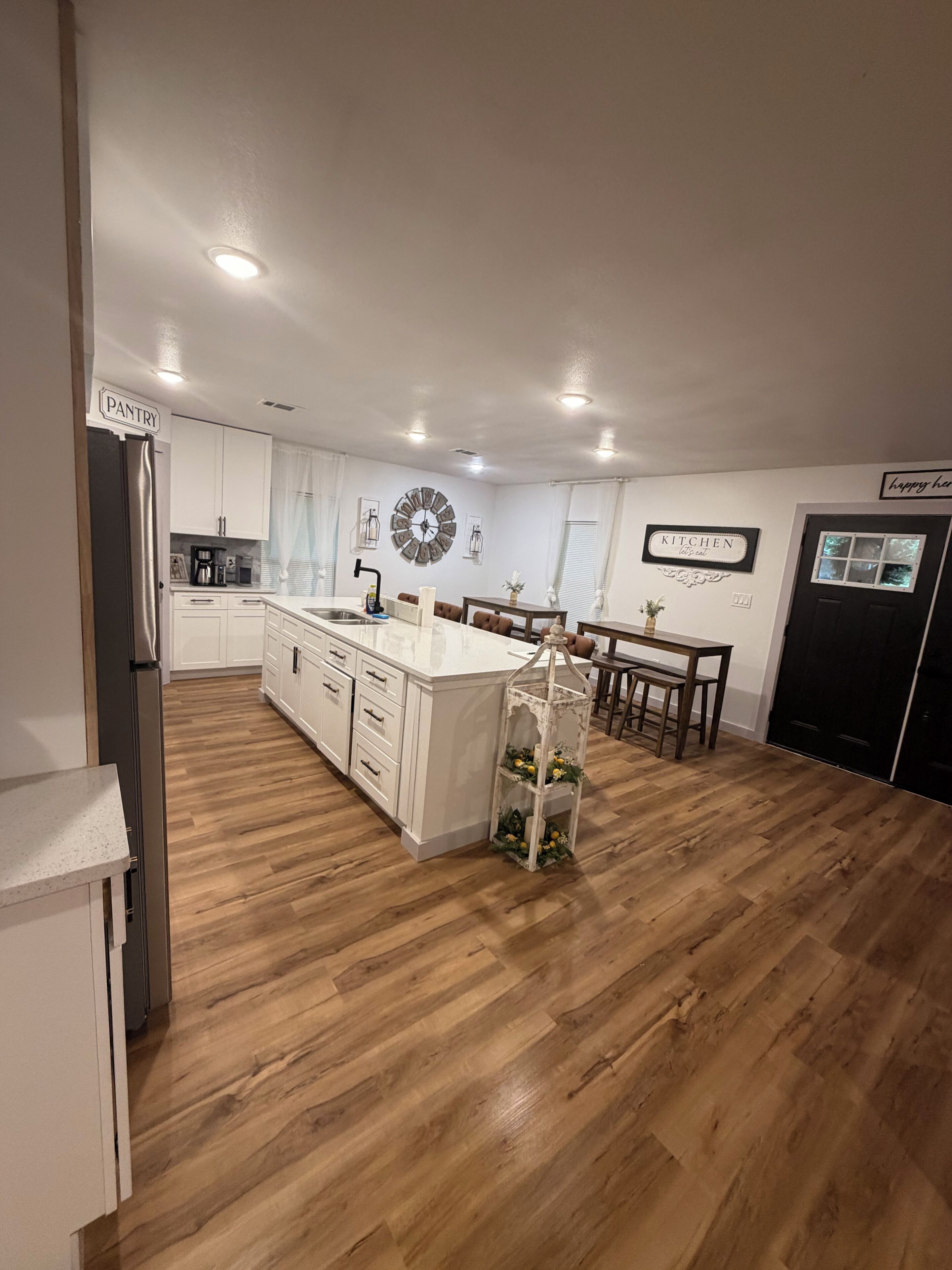 Una cocina moderna con armarios blancos, una isla central y un comedor con puerta negra.