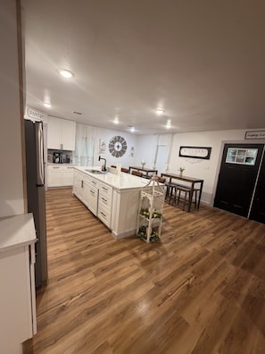 Una cucina moderna con mobili bianchi, un'isola centrale e un'area pranzo con una porta nera.