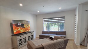 Una sala de estar con televisión, sofá y ventana.