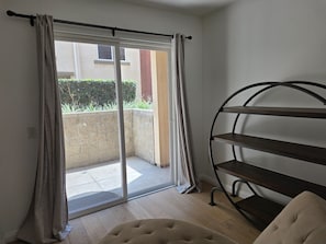 Ein Zimmer mit einer Schiebeglasdoor zum Balkon, einem Metallregal und einem Samtstuhl.