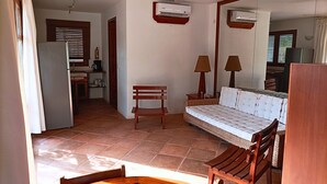 Ein Zimmer mit einem Bett, einer hölzernen Bank, einem Tisch, einem Deckenventilator und einer Klimaanlage.