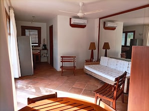 A room with a bed, a wooden bench, a table, a ceiling fan, and an air conditioning unit.