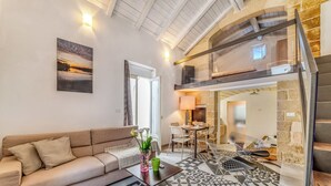 Ein modernes Wohnzimmer mit Sofa, Couchtisch und einem gemusterten Boden. Eine Treppe führt zu einer oberen Ebene mit einem Essbereich.