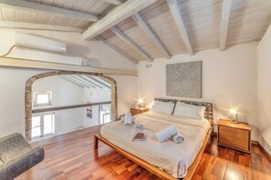 A bedroom with a wooden bed, a nightstand with a lamp, a large window, and a view of the sky. - Martano Jacuzzi Suite w/ Terrace & BBQ, Martano, Italy (Martano)