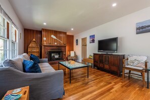 A living room with a fireplace, a sofa, a television, and wooden flooring.