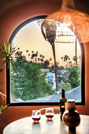 Ein Fenster mit Blick auf Palmen und Häuser, eine Flasche und zwei Gläser auf einem Tisch.