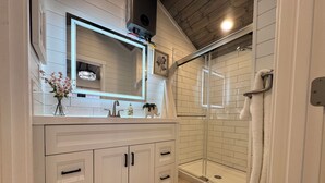 A bathroom with a white vanity, a large mirror, a shower with a glass door, and a towel rack. - Brand NEW Bungalow in Eatonville - Near Mt. Rainier (Eatonville)