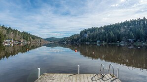 A wooden dock extending into calm water with a clear reflection of the surrounding forest and houses. - Brand NEW Bungalow in Eatonville - Near Mt. Rainier (Eatonville)