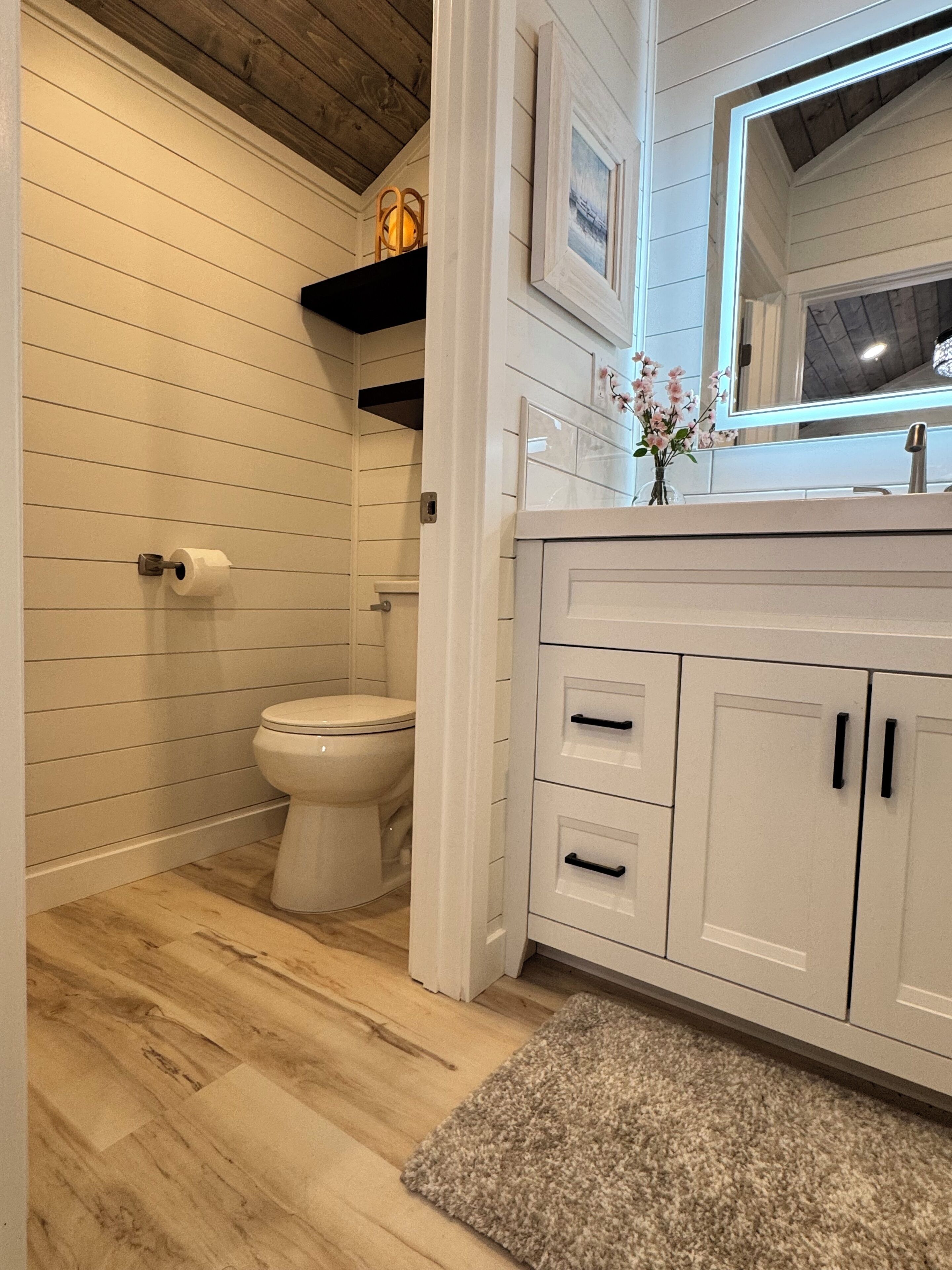 Une salle de bain avec des toilettes, un plancher en bois, des meubles blancs et un miroir.