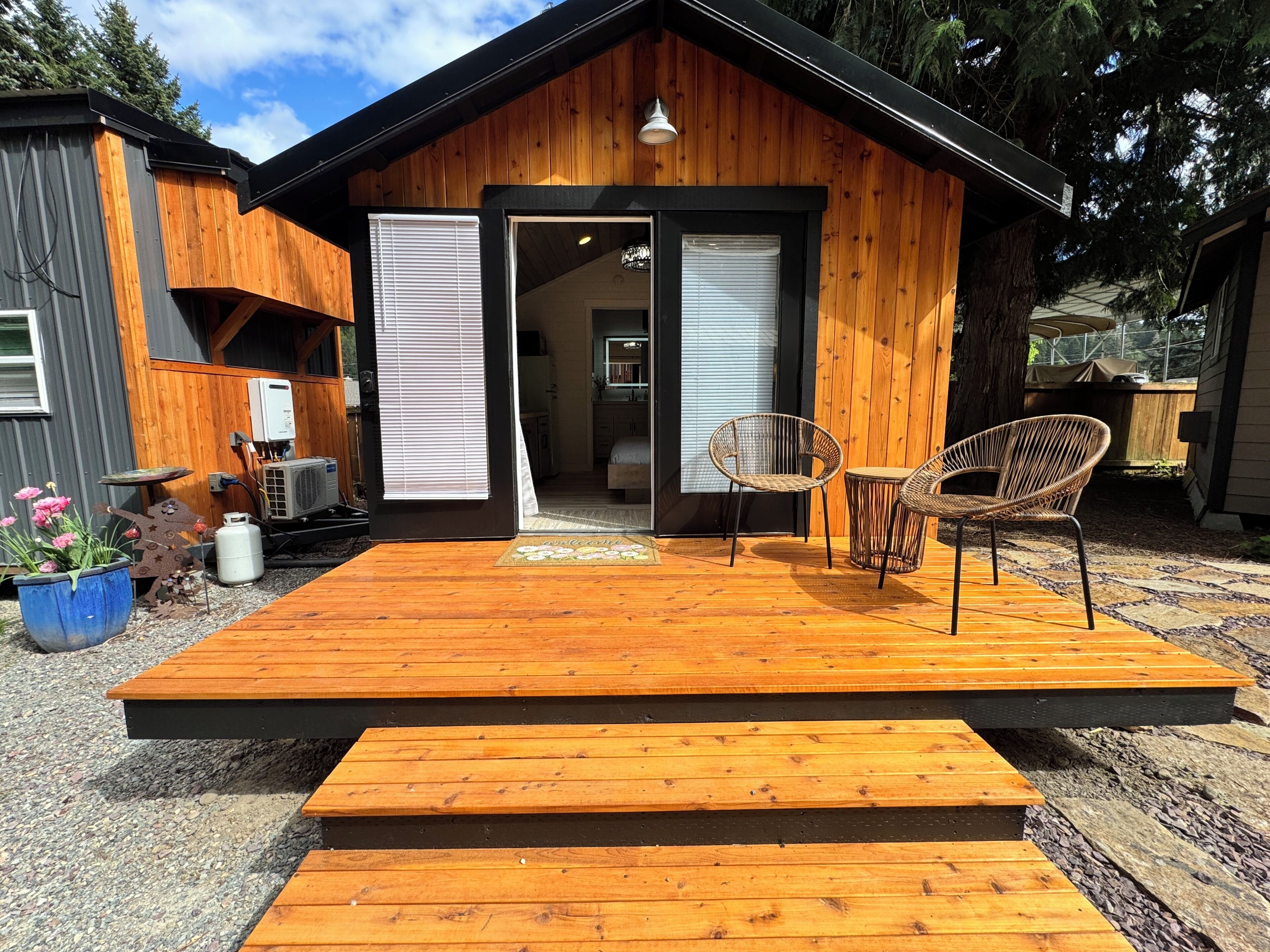 Une cabane en bois avec une terrasse, deux fauteuils en osier et un paillasson.