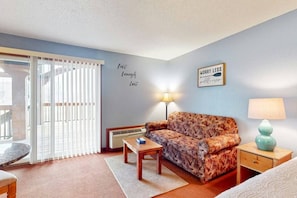 A cozy room with a patterned sofa, a small table, a lamp, and a bed.