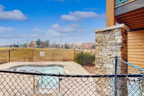 A fenced outdoor swimming pool with a stone wall and a wooden building in the background.