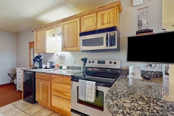 A kitchen with wooden cabinets, a microwave, an oven, a dishwasher, and a granite countertop.