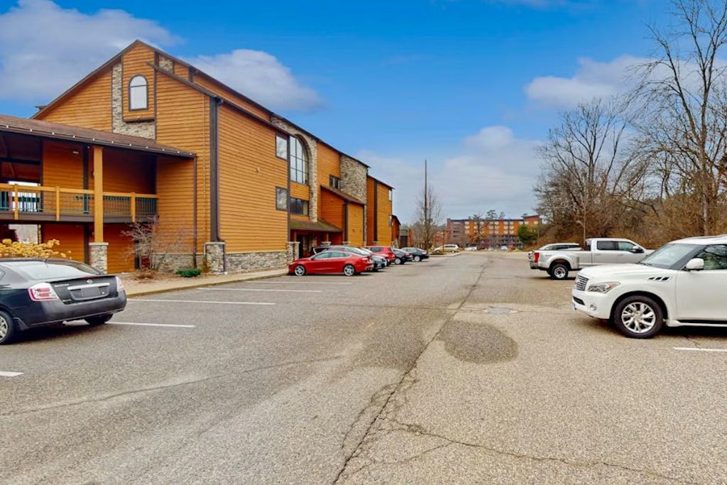 A building with a wooden facade, a balcony, and a parking lot with cars.
