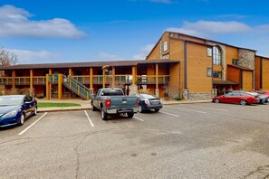 A building with a wooden facade, a staircase leading to a balcony, and a parking lot with several cars.