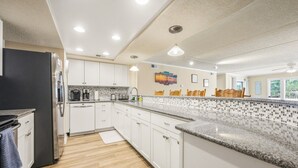 A modern kitchen with white cabinets, a granite countertop, and a black refrigerator. - Direct Ocean Front 3BR w/ Pool (Nags Head)