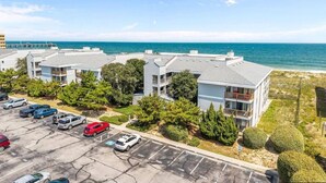 A coastal apartment building with parking, trees, and a view of the ocean. - Direct Ocean Front 3BR w/ Pool (Nags Head)