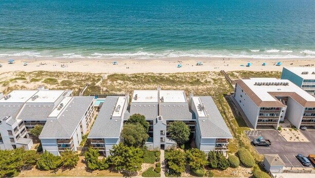 A beachfront hotel with multiple buildings, a sandy beach, and the ocean in the background. - Direct Ocean Front 3BR w/ Pool (Nags Head)