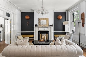A living room with a fireplace, a sofa, a coffee table, and a chandelier. - 
The Colonial Art House, Spacious 5BR Historic Gem (Alexandria)