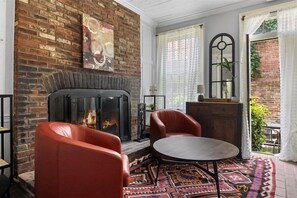 A cozy room with a brick fireplace, leather chairs, a round table, and a patterned rug. - 
The Colonial Art House, Spacious 5BR Historic Gem (Alexandria)