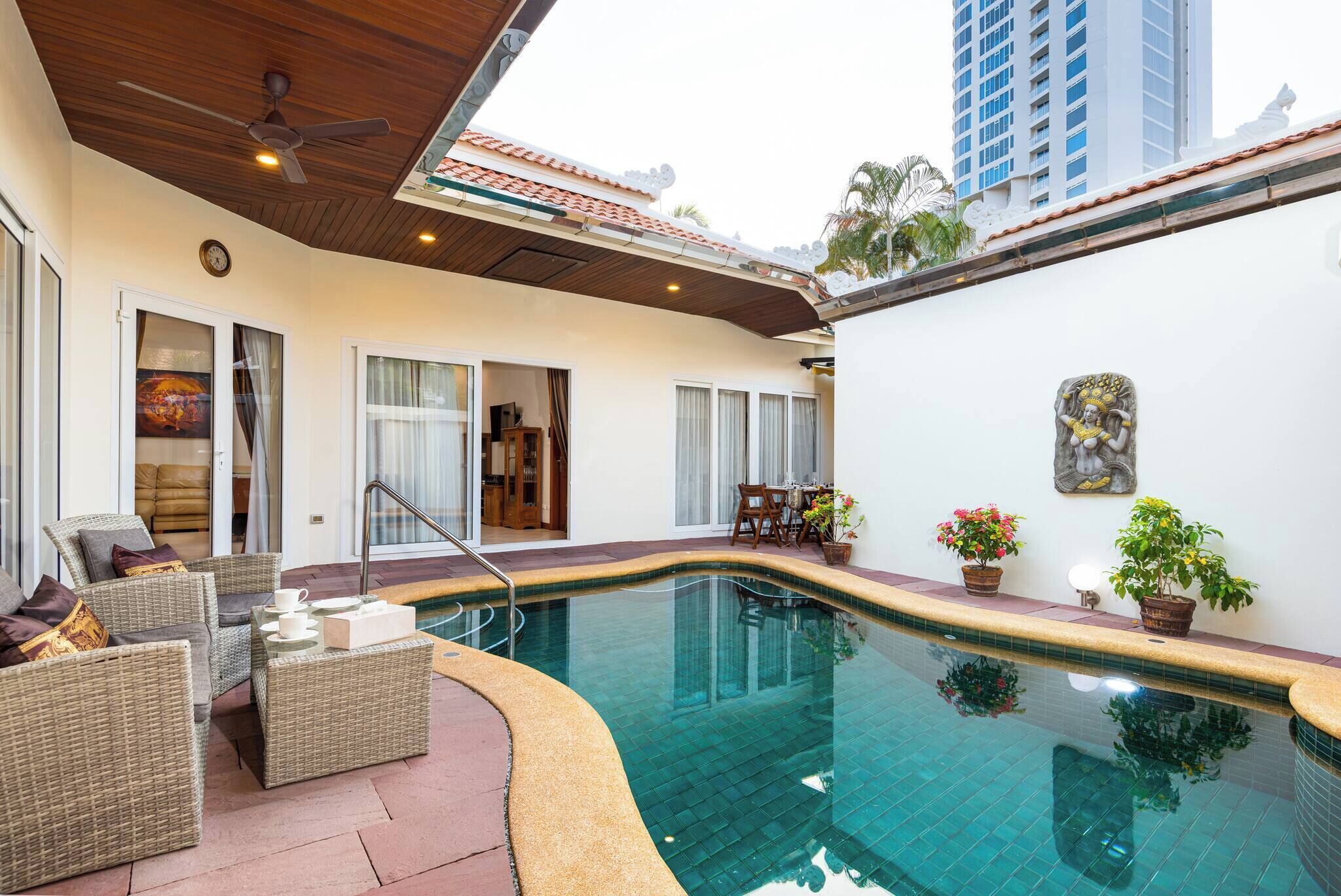 A swimming pool with a curved edge, wicker furniture, and a ceiling fan.