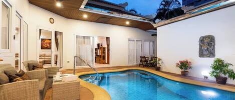 An indoor swimming pool with wicker furniture, a ceiling fan, and a clock on the wall.