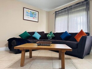 Un salon avec un canapé de couleur sombre, une table basse en bois et un tableau encadré accroché au mur.