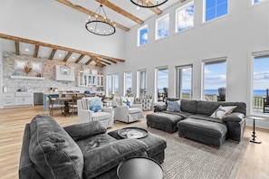 A spacious living area with a large sectional sofa, a dining table with chairs, and a kitchen in the background. - Beautiful 4BR Beachfront | Elevator + Game Room (Port Bolivar)