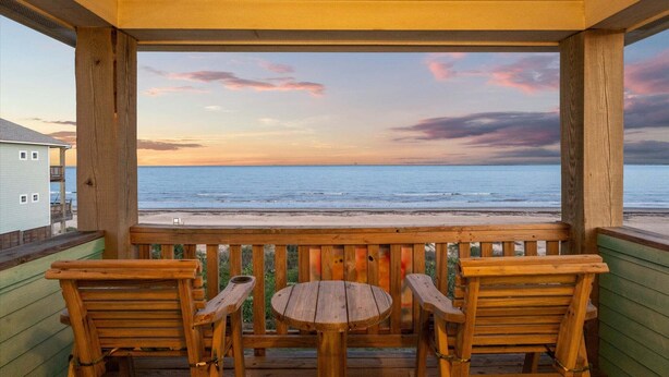 A wooden deck with a table and chairs, overlooking a beach and ocean. - Beachfront 5BR | Sleeps 16 | Fully Fenced Pet Friendly (Port Bolivar)