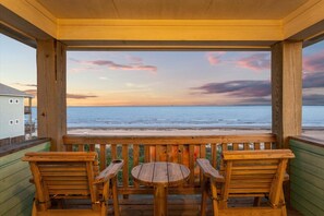 Eine Holzterrasse mit Tisch und Stühlen mit Blick auf Strand und Meer.