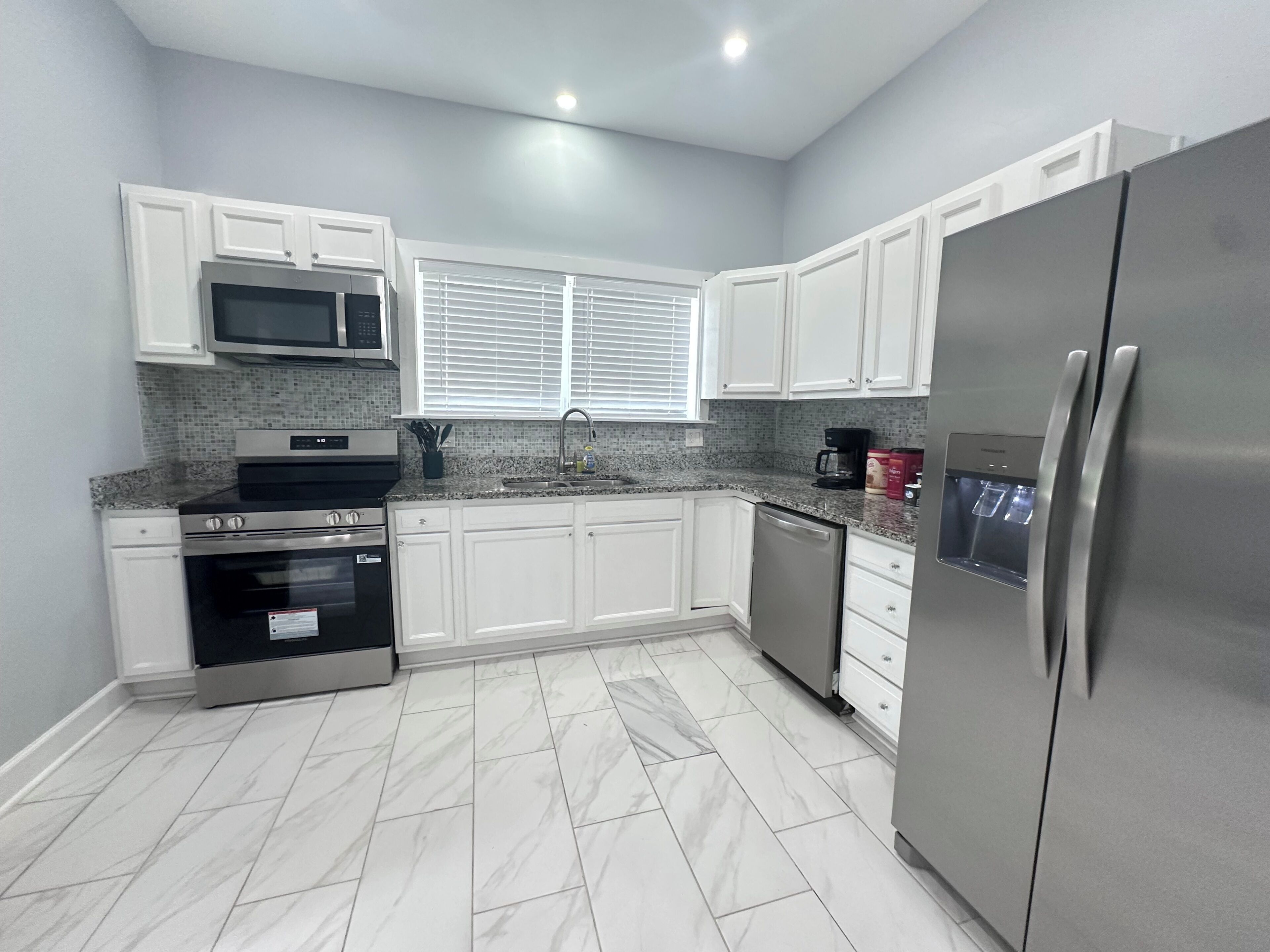 Una cocina moderna con armarios blancos, un refrigerador de acero inoxidable, un microondas, una estufa y un lavavajillas.