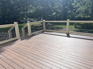 Eine Holzterrasse mit weißer Geländer, umgeben von viel Grün.