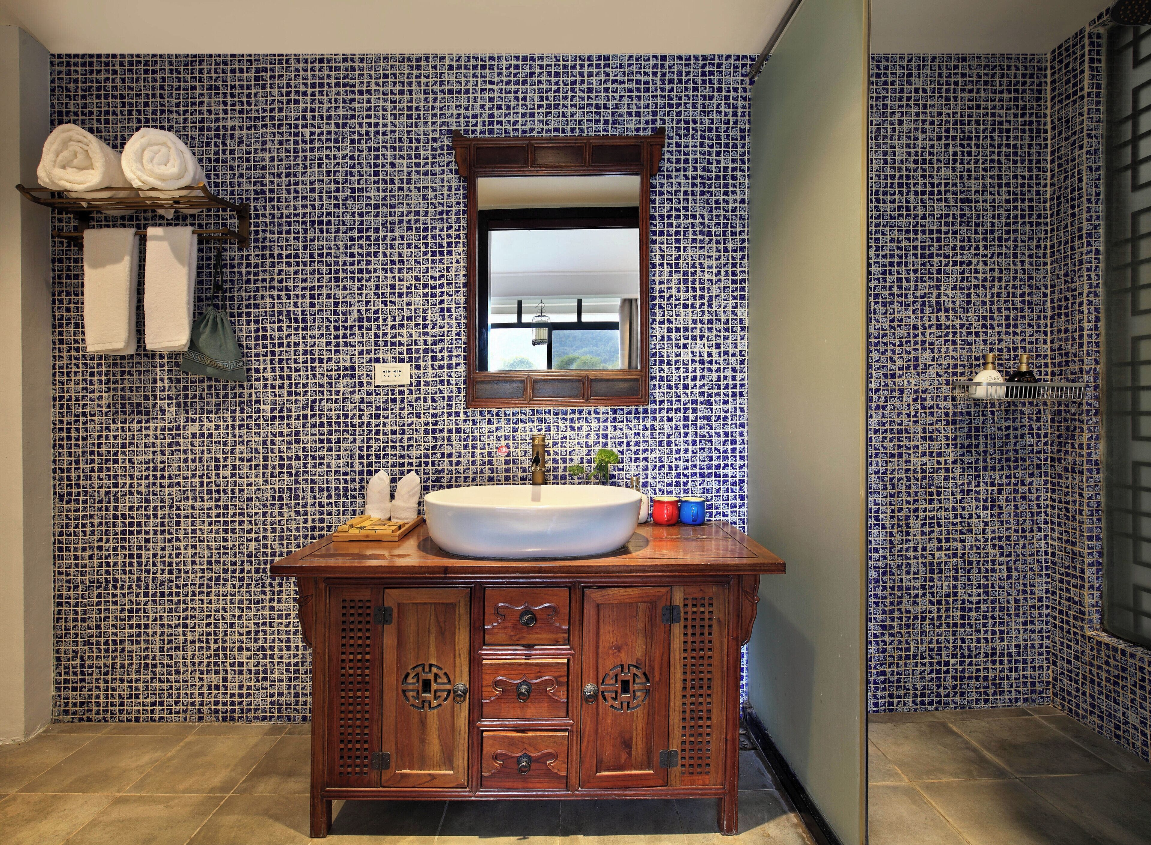 Casa de banho com lavatório, armário de madeira e azulejos estampados.