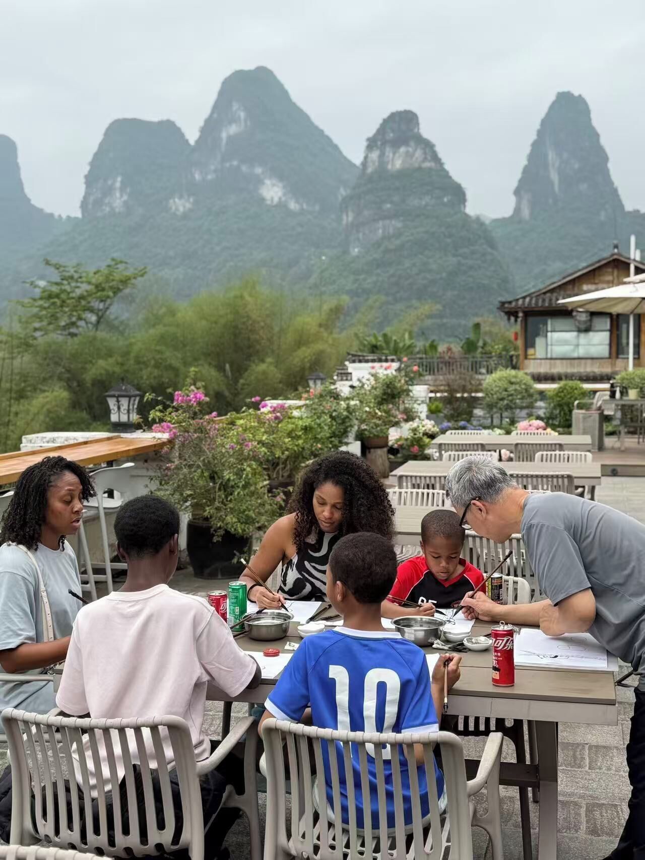 Eine Gruppe von Menschen speist an einem Tisch im Freien mit Blick auf eine Berglandschaft.