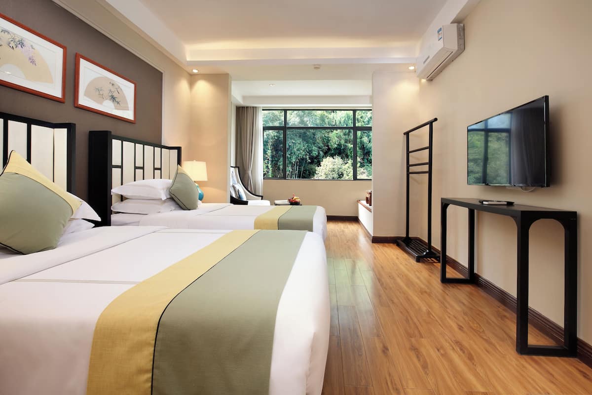 Habitación de hotel con dos camas, un televisor, ventana con vista a árboles y obras de arte enmarcadas en la pared.