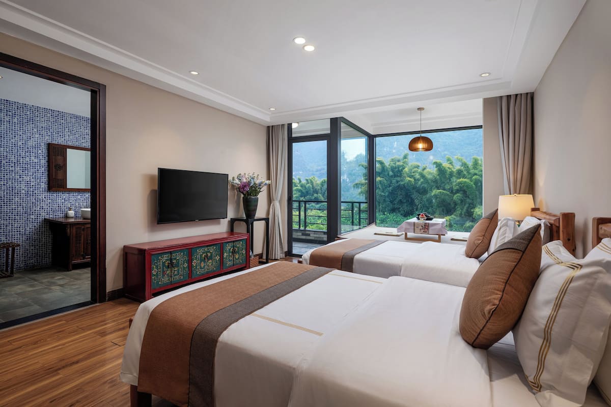 Habitación de hotel con dos camas, televisión, mueble de madera y balcón con vistas.