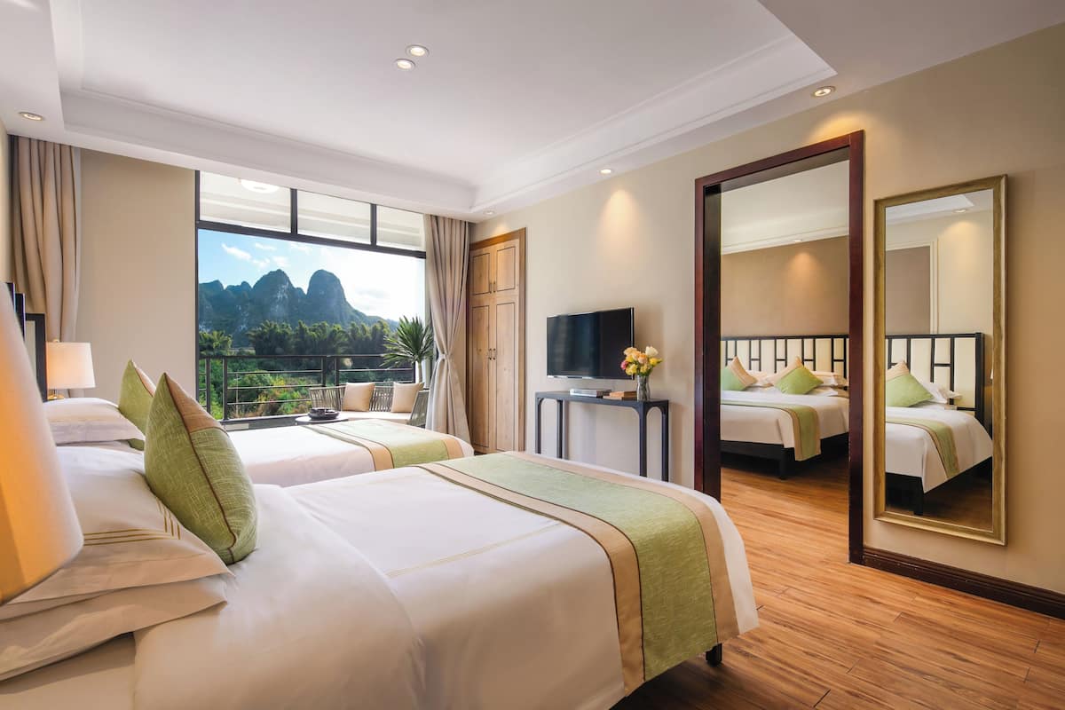 Habitación de hotel con dos camas, televisión, espejo y vistas a las montañas.