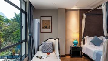 Habitación de hotel con cama, sofá, mesita de noche, lámpara y ventana con vistas a zonas verdes.