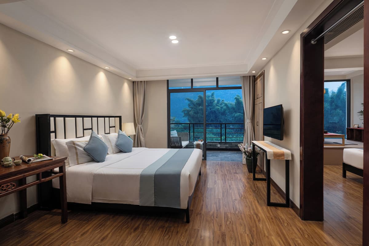 Habitación de hotel con cama, mesita de noche, televisión y balcón con vistas.